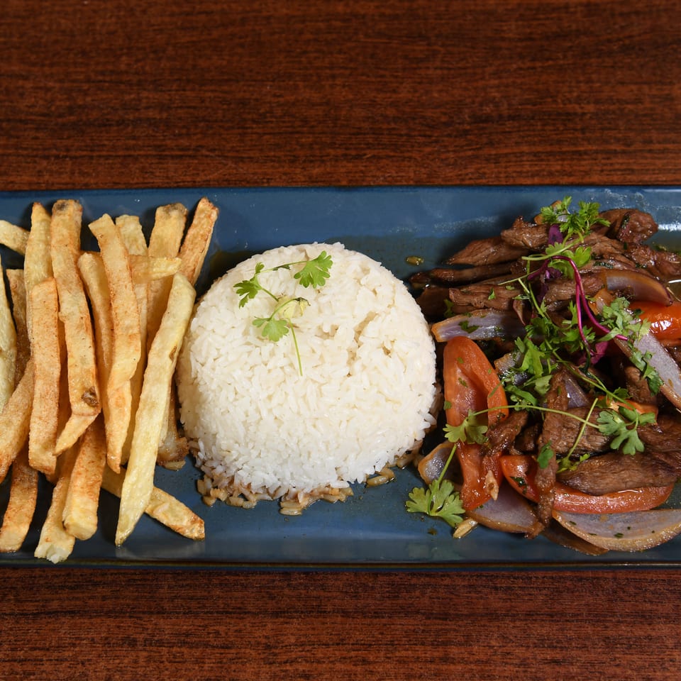 Blue platter with white rice, golden fries, and sautéed beef with tomatoes, onions, and herbs.