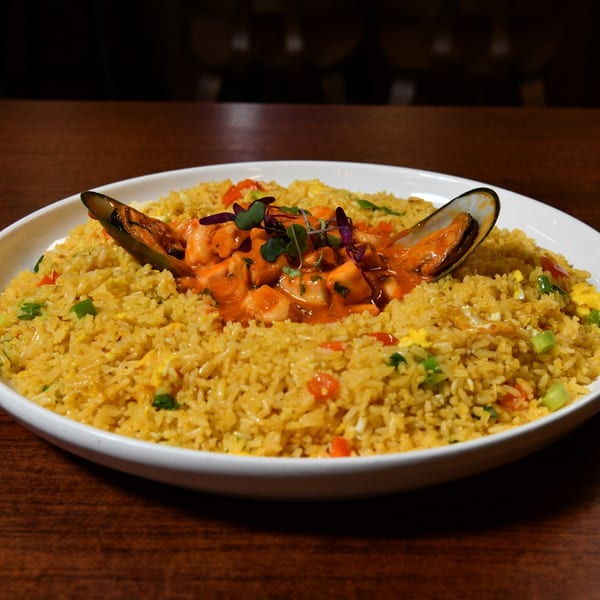 A white bowl of yellow fried rice with seafood in a red sauce and two mussels.